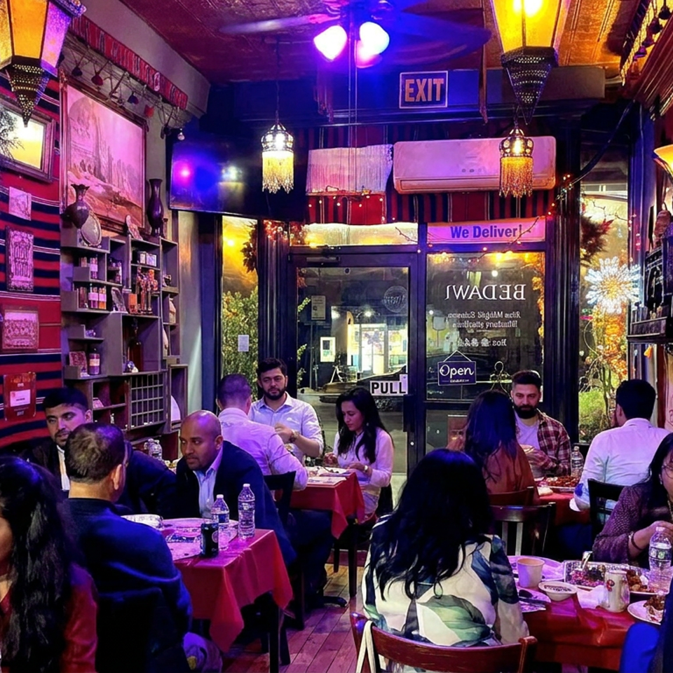 Bustling, richly decorated restaurant dining room with red tablecloths, ornate lighting, framed artwork, and multiple diners.